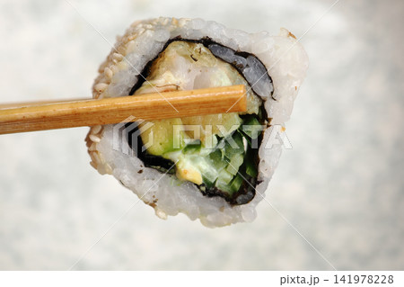 Sushi roll held with chopsticks in a dining setting Sushi roll held with chopsticks in a dining setting 141978228