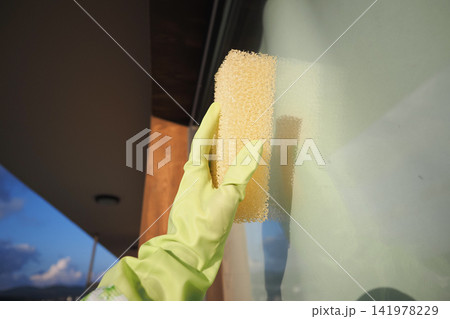 Cleaning a window with a sponge in bright daylight Cleaning a window with a sponge in bright daylight 141978229