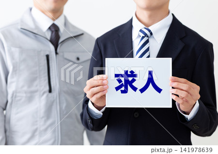 求人のホワイトボードを持つスーツを着た若い男性ビジネスマンと作業着のミドル男性 求人のホワイトボードを持つスーツを着た若い男性ビジネスマンと作業着のミドル男性 141978639