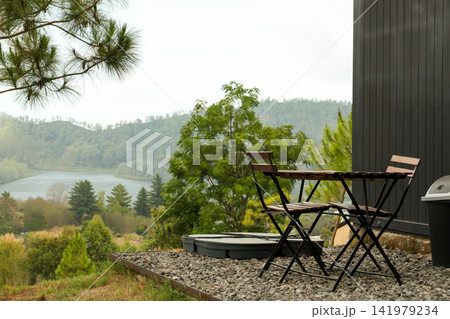 Cozy table and chairs set up beside the river surrounded by trees Cozy table and chairs set up beside the river surrounded by trees 141979234