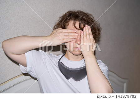 Woman Covering One Eye With Each Hand While Seated In Bedroom, Expressing Tiredness, Discomfort Woman Covering One Eye With Each Hand While Seated In Bedroom, Expressing Tiredness, Discomfort 141979782