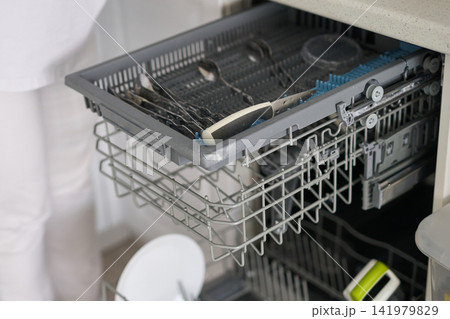 Person Loading Utensils Into Upper Cutlery Tray Of Open Dishwasher In Modern White Kitchen Near Person Loading Utensils Into Upper Cutlery Tray Of Open Dishwasher In Modern White Kitchen Near 141979829