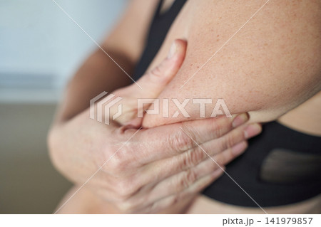 Middle-Aged Woman Holding Upper Arm In Discomfort During Indoor Closeup Self Examination In Sports Middle-Aged Woman Holding Upper Arm In Discomfort During Indoor Closeup Self Examination In Sports 141979857