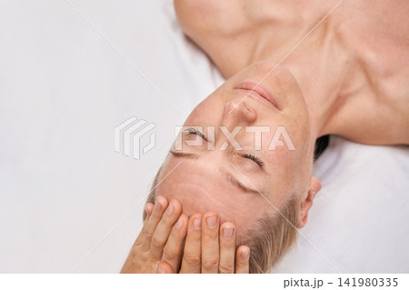 Female Client Resting During Facial Massage In Spa Treatment Room With Closeup View Of Relaxed Face Female Client Resting During Facial Massage In Spa Treatment Room With Closeup View Of Relaxed Face 141980335
