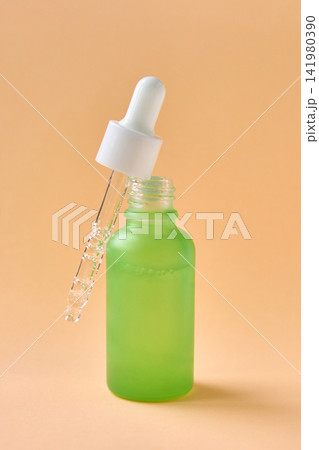 Green Frosted Dropper Bottle With Pipette Held Above Opening On Warm Orange Background, Cosmetic 141980390