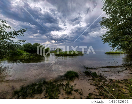 Storm Clouds Gathering Above Wide River And Sandy Shore 141982691