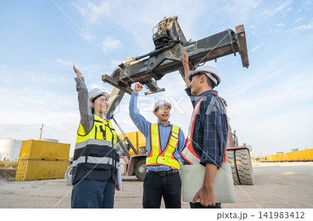 Construction team celebrating project success on job site with crane. 141983412