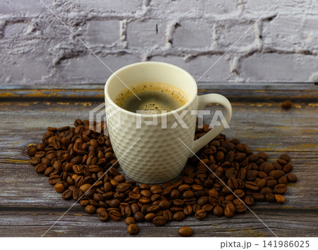 Warm coffee cup resting on a bed of roasted coffee beans in a cozy kitchen setting Warm coffee cup resting on a bed of roasted coffee beans in a cozy kitchen setting 141986025