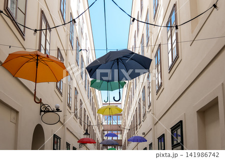 Colorful hanging umbrellas decorate a narrow European courtyard beneath blue sky Colorful hanging umbrellas decorate a narrow European courtyard beneath blue sky 141986742