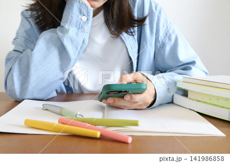 勉強に集中できずスマホを見る女性 勉強に集中できずスマホを見る女性 141986858