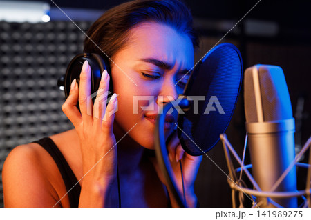 Female singer sings emotionally in the studio with her eyes closed Female singer sings emotionally in the studio with her eyes closed 141989275