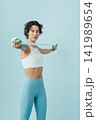 Slim woman with short hair practicing with a stretching band in a studio over blue background 141989654