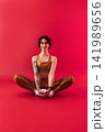 Young slim woman in golden fitness attire sitting on a crimson background 141989656