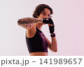 Slim woman with short hair wearing gloves practicing shadow punches in a studio 141989657