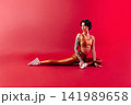 Woman doing stretching exercises over a crimson background in a studio 141989658