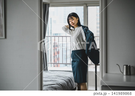 ビジネスウーマンが部屋でジャケットを羽織り出社準備をする 身支度をする 度る 羽織る様子、出社準備 ビジネスウーマンが部屋でジャケットを羽織り出社準備をする 身支度をする 度る 羽織る様子、出社準備 141989868