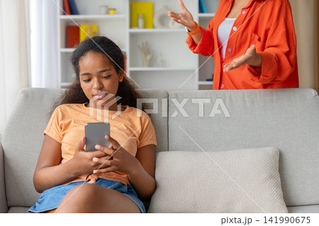 Teenage girl ignoring mothers gestures while focused on her smartphone Teenage girl ignoring mothers gestures while focused on her smartphone 141990675