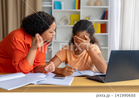 Upset black daughter covering eyes while frustrated mother explaining homework problem Upset black daughter covering eyes while frustrated mother explaining homework problem 141990688