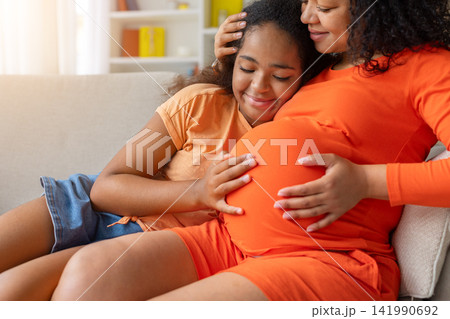 Closeup of black daughter resting against pregnant mothers belly, both smiling 141990692