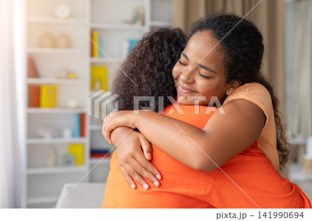 Young Black daughter hugging her mother tightly at home with peaceful smile 141990694