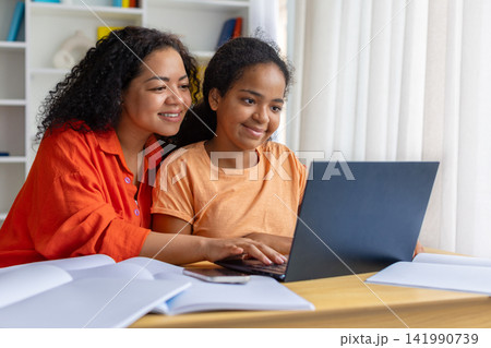 Smiling black mother helping daughter with homework on laptop Smiling black mother helping daughter with homework on laptop 141990739