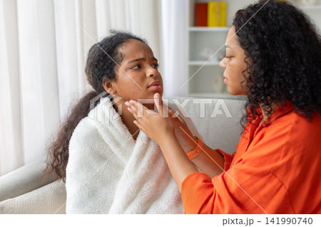 Black mother examining daughter's throat and glands, checking for swelling 141990740