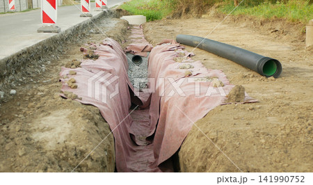 Road construction new sewer pipe drainage installation roadway roadwork, long trench excavated channel, excavation site preparation road repair gravel bedding and geotextile fabric, corrugated pipe Road construction new sewer pipe drainage installation roadway roadwork, long trench excavated channel, excavation site preparation road repair gravel bedding and geotextile fabric, corrugated pipe 141990752