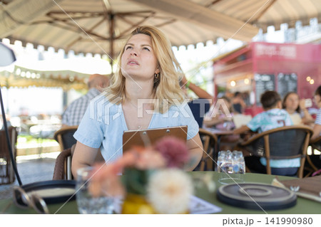 Woman looks up in outdoor cafe while holding a menu during afternoon lunch Woman looks up in outdoor cafe while holding a menu during afternoon lunch 141990980