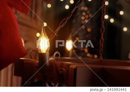 warm glowing filament bulb illuminates rustic chandelier soft blurred Christmas lights bokeh background warm glowing filament bulb illuminates rustic chandelier soft blurred Christmas lights bokeh background 141991441