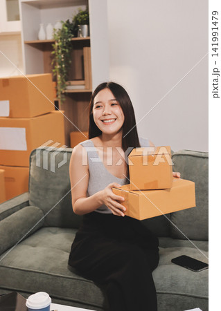 Startup SME small business entrepreneur of freelance Asian woman wearing apron using laptop and box to receive and review orders online to prepare to pack sell to customers, online sme business ideas. 141991479