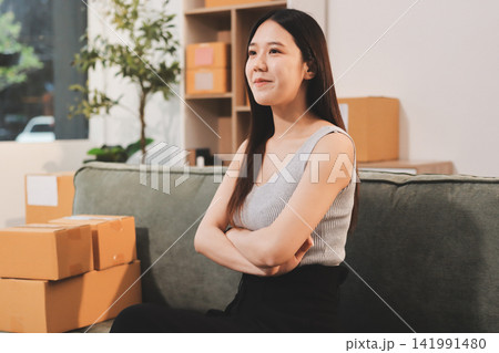 Startup SME small business entrepreneur of freelance Asian woman wearing apron using laptop and box to receive and review orders online to prepare to pack sell to customers, online sme business ideas. Startup SME small business entrepreneur of freelance Asian woman wearing apron using laptop and box to receive and review orders online to prepare to pack sell to customers, online sme business ideas. 141991480