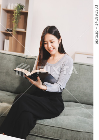 Young woman reading book on sofa at home Young woman reading book on sofa at home 141991533
