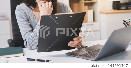 Young Asian woman sits at office desk rubbings her eyes and temples feeling pain. Stress. And exhaustion from long hours working on the computer Young Asian woman sits at office desk rubbings her eyes and temples feeling pain. Stress. And exhaustion from long hours working on the computer 141991547