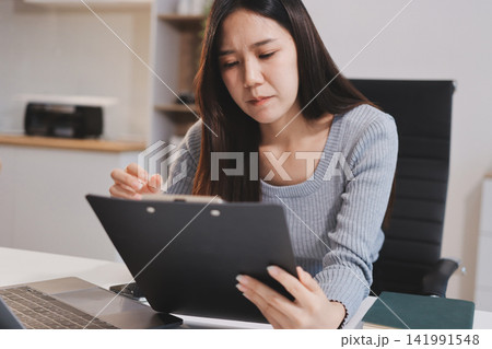 Young Asian woman sits at office desk rubbings her eyes and temples feeling pain. Stress. And exhaustion from long hours working on the computer Young Asian woman sits at office desk rubbings her eyes and temples feeling pain. Stress. And exhaustion from long hours working on the computer 141991548