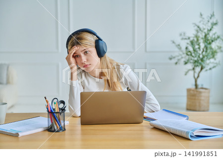 Tired teenage girl in headphones studying with laptop Tired teenage girl in headphones studying with laptop 141991851