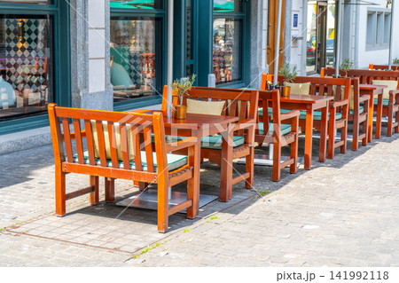 Wooden Chairs and Tables on old Street Outside Cozy European Restaurant Terrace in summer Wooden Chairs and Tables on old Street Outside Cozy European Restaurant Terrace in summer 141992118