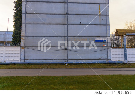 Industrial concrete wall with pipeline and fenced perimeter under soft daylight outdoors Industrial concrete wall with pipeline and fenced perimeter under soft daylight outdoors 141992659