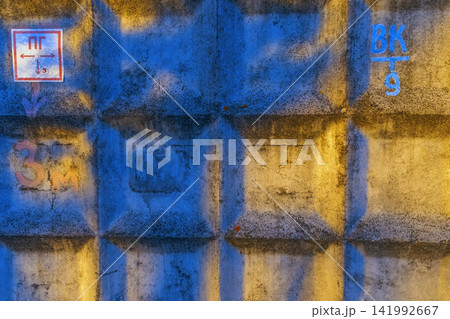 Weathered concrete wall with geometric recessed panels lit by blue and golden light creating high contrast texture Weathered concrete wall with geometric recessed panels lit by blue and golden light creating high contrast texture 141992667
