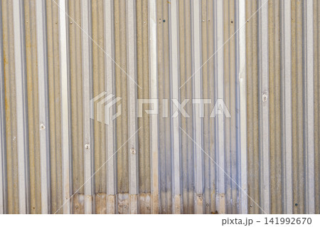 Weathered corrugated metal wall with vertical ridges, rust stains, bolted panels, and faded industrial tones Weathered corrugated metal wall with vertical ridges, rust stains, bolted panels, and faded industrial tones 141992670
