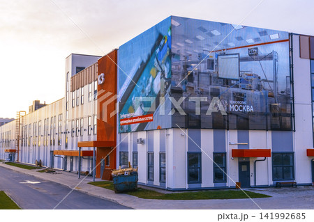 Modern industrial building exterior with giant corner mural, white facade, orange accents, and empty street at dusk 141992685