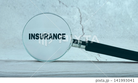 A magnifying glass shows the word insurance on a wooden table with a light background 141993041