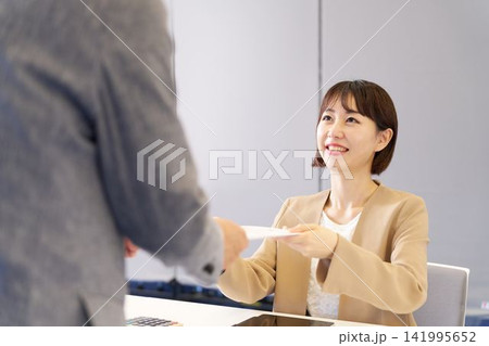 来客に資料を差し出す受付の女性スタッフ 来客に資料を差し出す受付の女性スタッフ 141995652