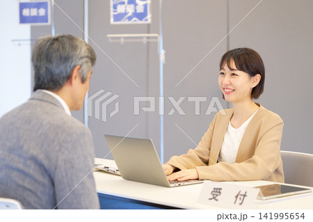 相談会の受付で来場者に笑顔で応対する女性スタッフ 141995654