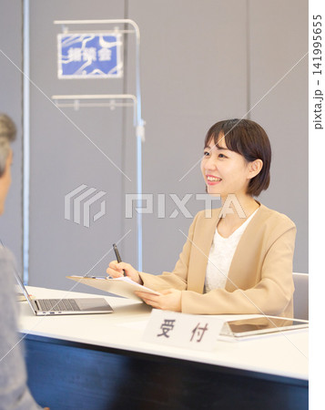 相談会の受付で来場者に笑顔で応対する女性スタッフ 141995655