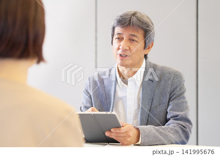 タブレットを手に穏やかに説明するシニア男性相談員 タブレットを手に穏やかに説明するシニア男性相談員 141995676