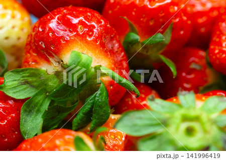 Fresh red strawberries with green leaves arranged closely, showcasing their vibrant color and texture against a blurred background 141996419