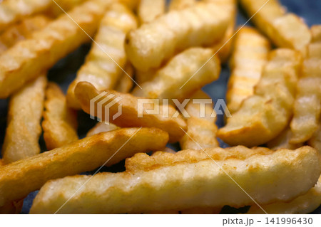 Crispy golden crinkle-cut French fries piled on a blue plate, showcasing their textured surface and appetizing appearance in a close-up view Crispy golden crinkle-cut French fries piled on a blue plate, showcasing their textured surface and appetizing appearance in a close-up view 141996430