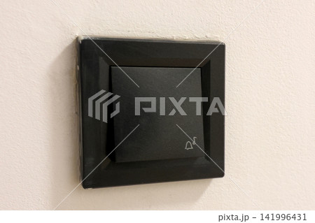 Black electrical switch mounted on a white wall with a textured surface, featuring a square design and subtle markings for functionality Black electrical switch mounted on a white wall with a textured surface, featuring a square design and subtle markings for functionality 141996431