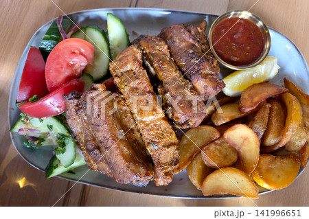 Delicious Grilled Ribs with Potato Wedges, Fresh Salad, and Savory Dip Delicious Grilled Ribs with Potato Wedges, Fresh Salad, and Savory Dip 141996651