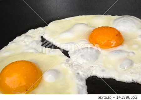 Close-Up of Two Sunny-Side Up Eggs Sizzling in a Black Frying Pan for Breakfast Close-Up of Two Sunny-Side Up Eggs Sizzling in a Black Frying Pan for Breakfast 141996652